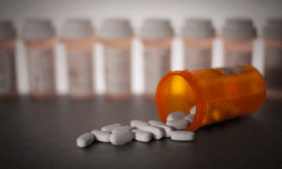 Orange pill bottle fallen over a table with its contents, white pills, strewn over the table surface.